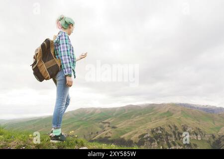 A hipster girl traveled by a blogger in a plaid shirt and with multi-colored hair using a compass standing on a plateau background in the mountains Stock Photo