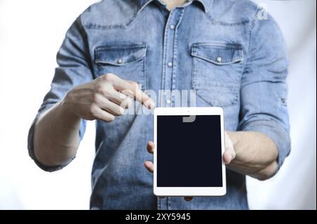 Casual man in denim shirt showing digital tablet computer screen in hands. Isolated on white. Clipping path for display included. He points a finger a Stock Photo