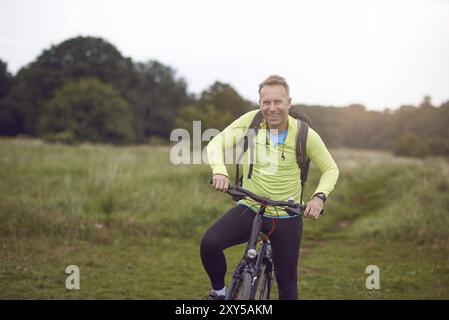 Smiling mature man wearing sportswear on bicycle tour through meadow Stock Photo