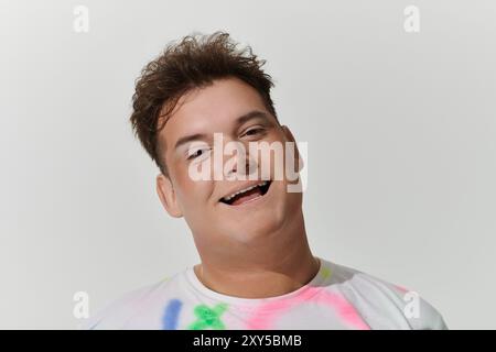 A queer person with brown hair smiles brightly while wearing a colorful tie-dye shirt. Stock Photo