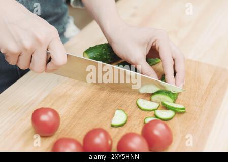 Close-up of female hands cut into fresh cut cucumbers on a wooden cutting board next to pink tomatoes. The concept of homemade vegetarian cuisine and Stock Photo