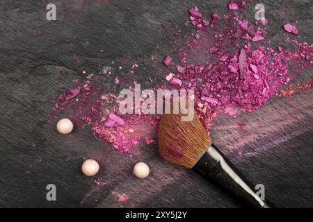 A closeup of a makeup brush with vibrant pink and purple eye shadow, shot from above on a black texture with copy space Stock Photo