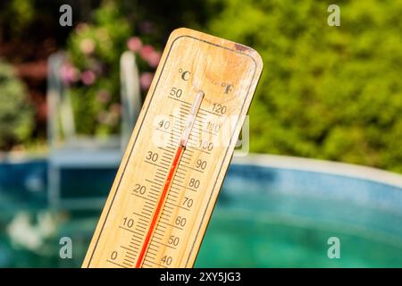 Thermometer displaying high summer temperature on a swimming pool background Stock Photo