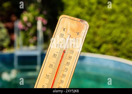 Thermometer displaying high summer temperature on a swimming pool background Stock Photo