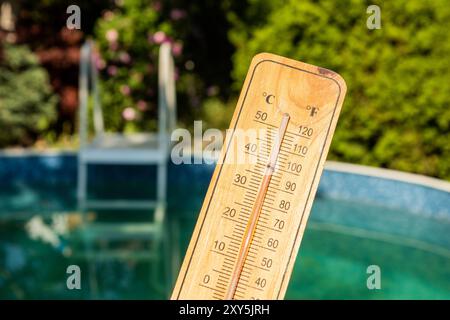 Thermometer showing almost 40 degrees celsius held above a swimming pool Stock Photo