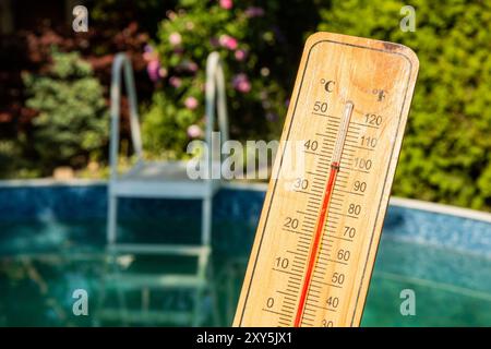 Thermometer displaying high summer temperature on a swimming pool background Stock Photo