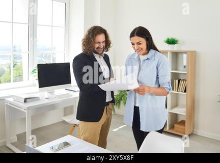 Two business people man and woman standing in office and looking through financial documents. Stock Photo