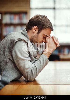 Man, praying and spiritual in university for study, worship and college scholarship in library. Student, faith and meditation to God on campus for Stock Photo