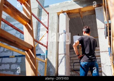 Back view of man architect engineer checking house under construction comparing with blueprint plan on paper. Gas block Stock Photo
