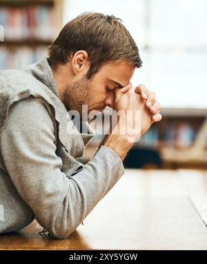 Student, praying and spiritual in university for study, worship and college scholarship in library. Man, faith and meditation to God on campus for Stock Photo