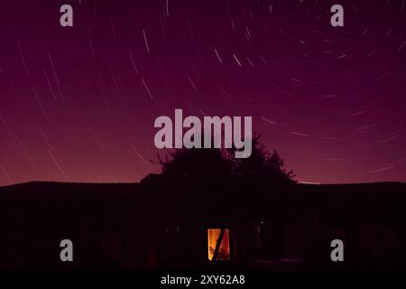 Star trails in the night sky over an old house and tree in the countryside Stock Photo