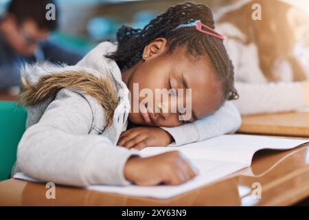 Black girl, tired and student sleeping on desk, bored child and learner dreaming in classroom. Female person, fatigue and burnout for education or Stock Photo