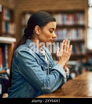 Student, praying and spiritual on campus for study, worship or college scholarship in library. Woman, learning and meditation to God in university for Stock Photo