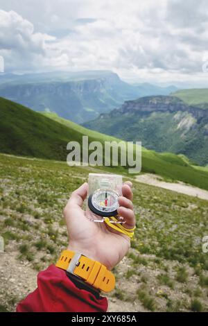 Male hand is holding a magnetic compass on the background of hills and the sky with clouds. The concept of traveling and finding your life path Stock Photo