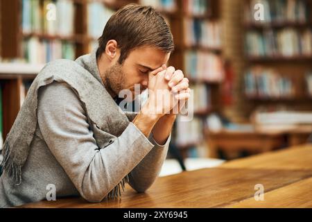 Student, praying and spiritual in college for study, worship and university scholarship in library. Man, faith and meditation to God on campus for Stock Photo