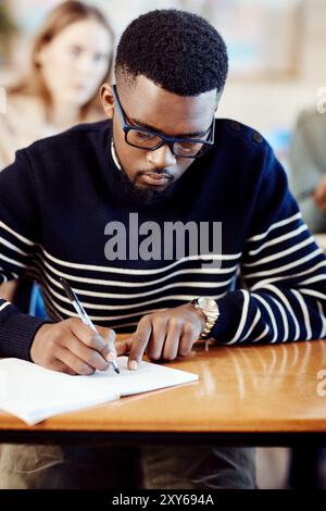 Student, writing and man learning in exam class for education, knowledge or test preparation in college. University, guy and studying with book for Stock Photo
