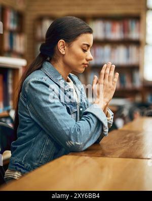 Student, praying and learning in university for study, worship and college scholarship in library. Woman, faith and meditation to God on campus for Stock Photo