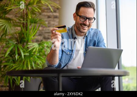 Low angle view of positive male entrepreneur transferring money with laptop and credit card in office Stock Photo