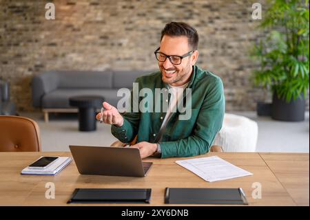 Male computer programmer smiling and discussing project details over video call on laptop in office Stock Photo