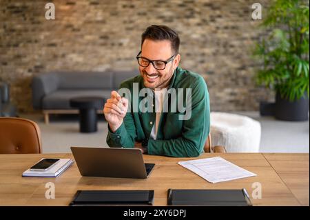 Smiling male programmer in eyeglasses looking at computer while designing website at desk in office Stock Photo