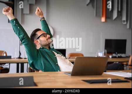 Male professional with laptop on desk stretching hands and relaxing at his workplace during break time Stock Photo