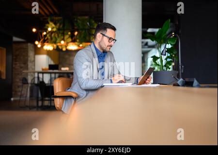 Focused young businessman with eyeglasses and notepad working over laptop at his workplace in office Stock Photo