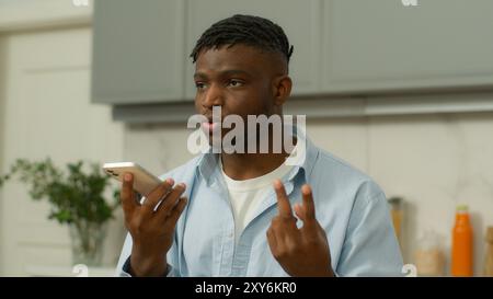 African American man serious biracial male hold smartphone using speaker phone speaking talk to cellphone loudspeaker comfort usage counting with Stock Photo
