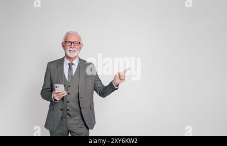 Senior male manager with mobile phone pointing at copy space and advertising over white background Stock Photo