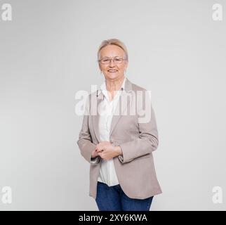 Confident elderly female entrepreneur with eyeglasses and hands clasped posing on white background Stock Photo