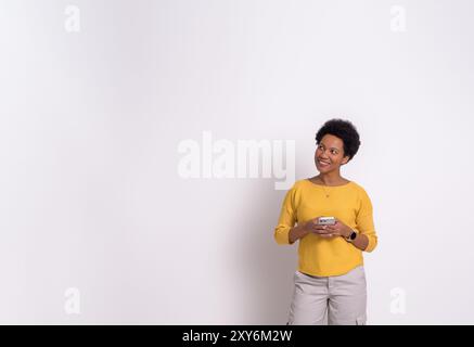 Thoughtful female professional holding smart phone and looking away on isolated white background Stock Photo