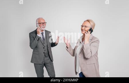 Confident senior business partners talking over mobile phones while standing over white background Stock Photo
