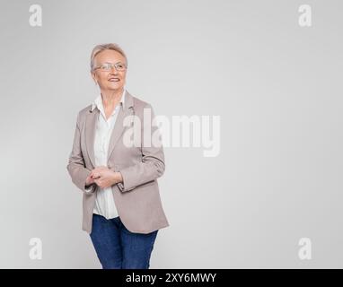 Confident old female CEO with hands clasped contemplating and looking away over white background Stock Photo