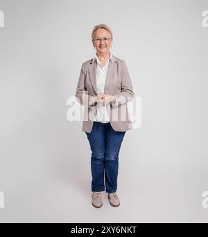 Portrait of smiling confident senior businesswoman with hands clasped standing on white background Stock Photo
