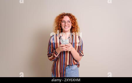 Excited female entrepreneur with curly hair using social media on smart phone over white background Stock Photo