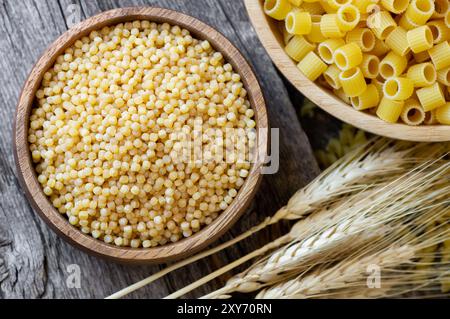 Raw couscous in bowl on wooden background with wheats, uncooked food concept Stock Photo