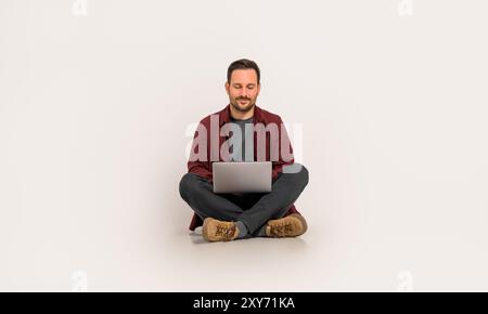 Full length of handsome entrepreneur checking e-mails over laptop while sitting on white background Stock Photo