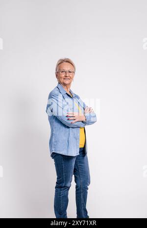 Portrait of smiling old businesswoman in eyeglasses and with arms crossed posing on white background Stock Photo