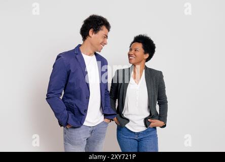 Happy young coworkers with hands in pockets looking at each other while standing on white background Stock Photo
