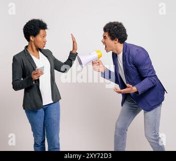 Furious businesswoman showing stop sign to man shouting at her with megaphone on white background Stock Photo