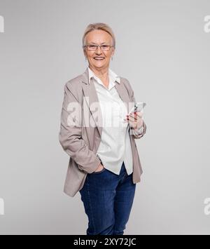Portrait of confident senior female professional smiling and using mobile phone on white background Stock Photo