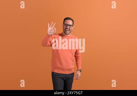 Portrait of handsome ecstatic manager showing OK sign and laughing on isolated orange background Stock Photo