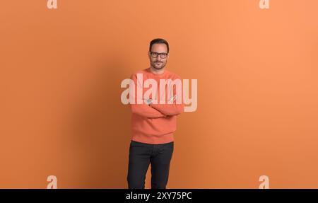 Portrait of handsome young businessman in eyeglasses with arms crossed posing on orange background Stock Photo