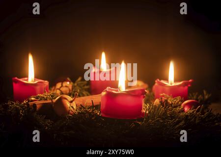 Decorated Advent wreath made of fir branches with burning red candles against a black background Stock Photo