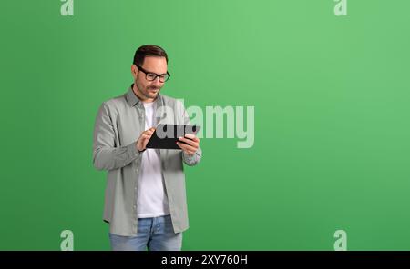 Focused young businessman doing online research over digital tablet on isolated green background Stock Photo