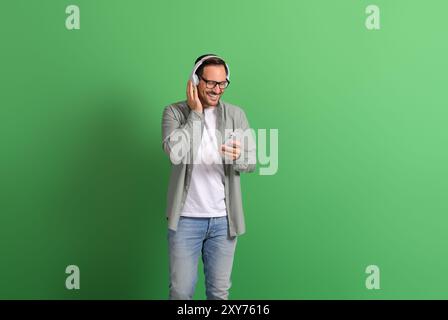 Smiling young man using mobile phone and answering calls over headphones on green background Stock Photo
