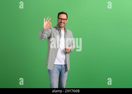 Portrait of satisfied handsome customer smiling and showing OK sign on isolated green background Stock Photo