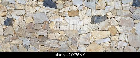 Bright natural stone wall cladding with single dark stones on a facade Stock Photo