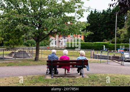 Rear view of three elderly people all with white hair two women one man sitting on a bench by the riverside at Shepperton lock Surrey England UK Stock Photo