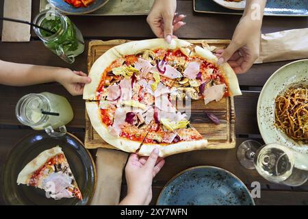 Concept of friendly family dinner party preparation. Top view. Horizontal, dinner with pizza, pasta, white wine and lemonade Stock Photo