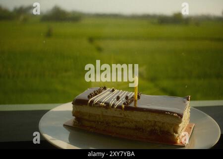 Chocolate cheese birthday cake and candles on a white plate with a rice field view Stock Photo